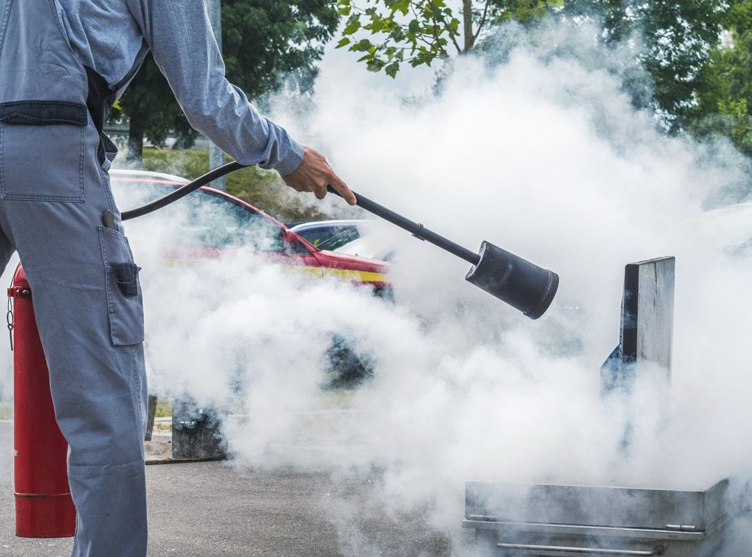 Brandschutzunterweisung der KLB-Mitarbeiter mittels eines brennenden Behälters im Vordergrund
