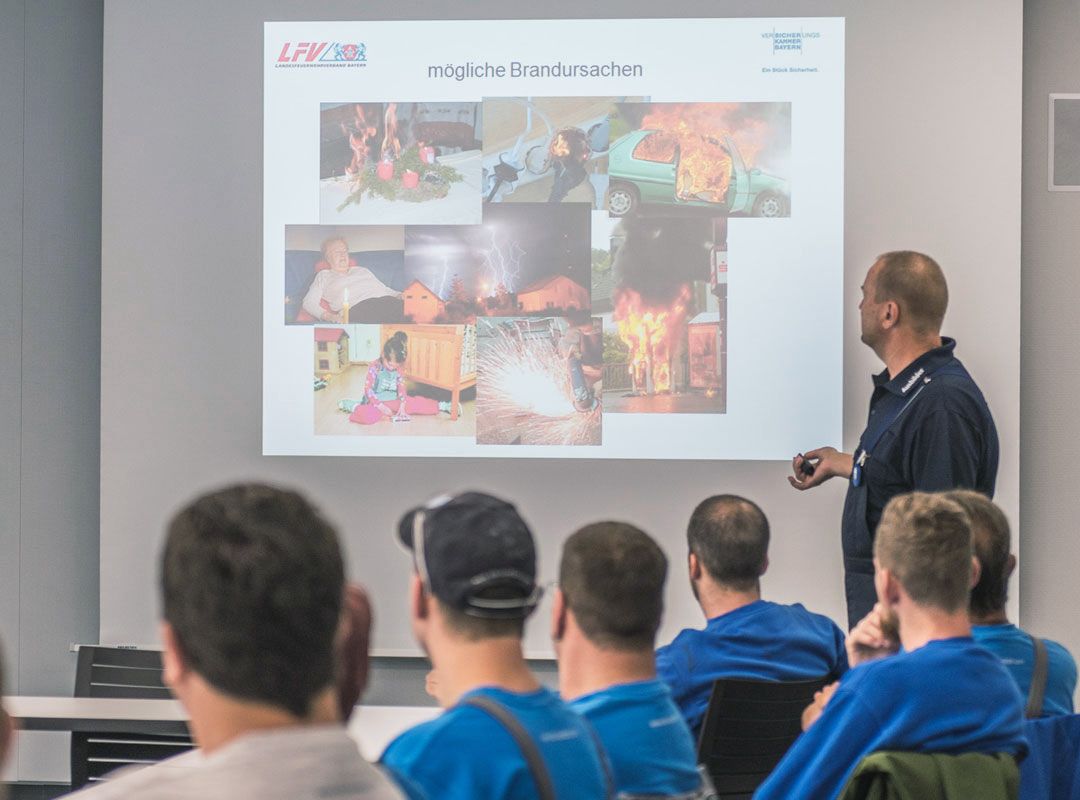 Brandschutzunterweisung der KLB-Mitarbeiter mittels eines brennenden Behälters im Vordergrund
