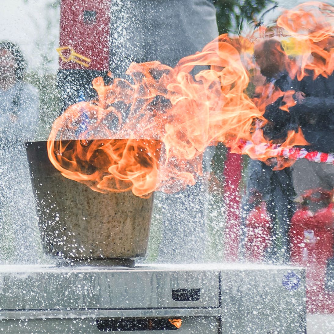 Brandschutzunterweisung der KLB-Mitarbeiter mittels eines brennenden Behälters im Vordergrund