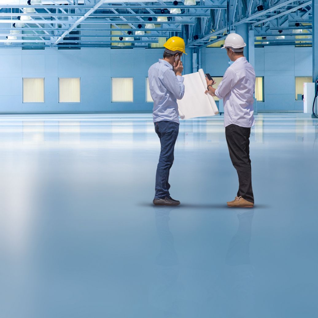 Weitläufige, beschichtete Halle mit zwei Bauherren mit einem Plan in der Hand