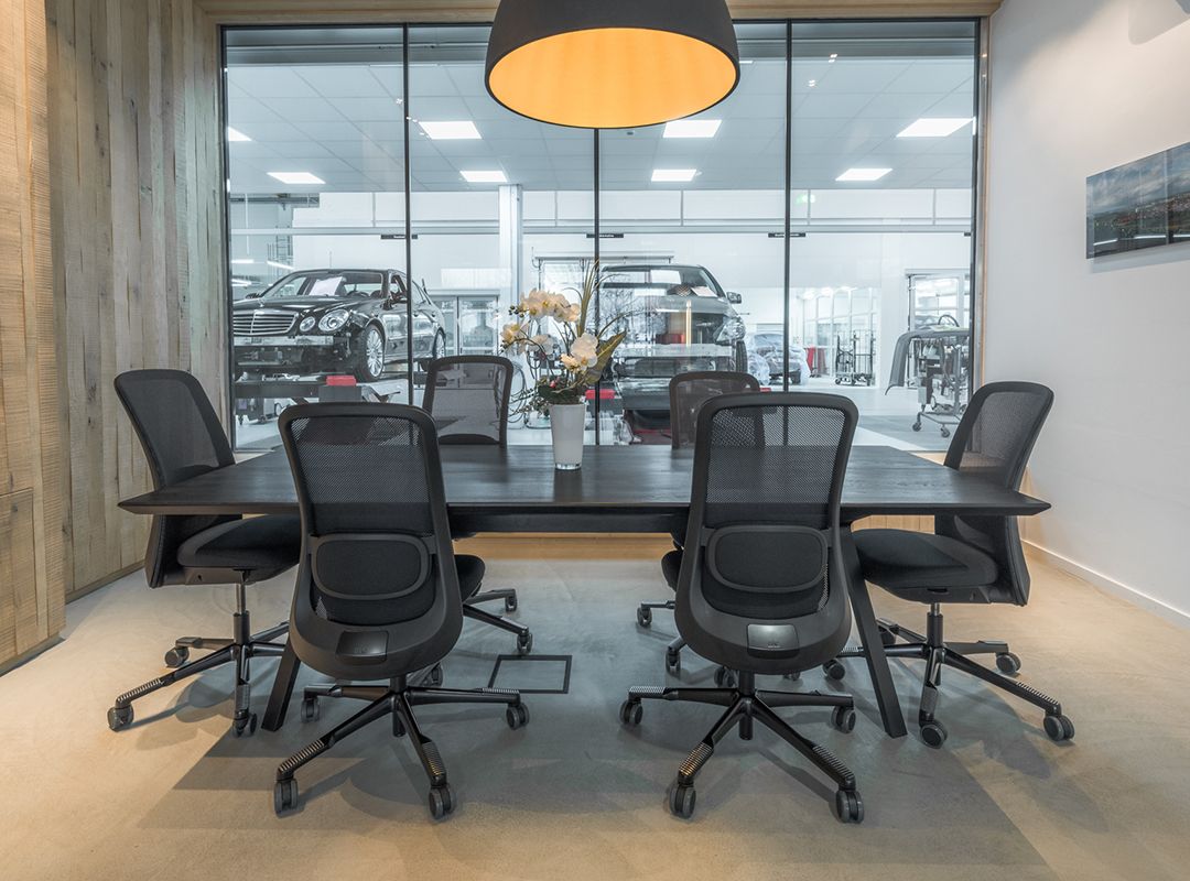 Beschichteter Besprechungsraum mit großer Glasfront mit Einblick in die Werkstatt, in der Autos auf Hebebühnen zu sehen sind