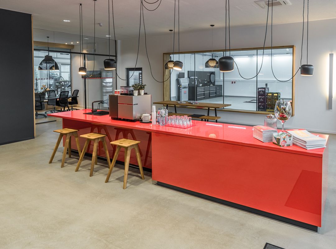 Dekorative, rote Küche im Empfangsbereich mit dezentem Spachtelboden und einem Büro und einer Werkstatt im Hintergrund